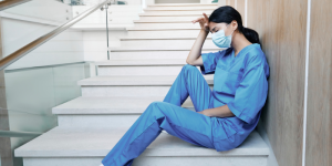Tired nurse resting on stairs with her hand to her forehead.